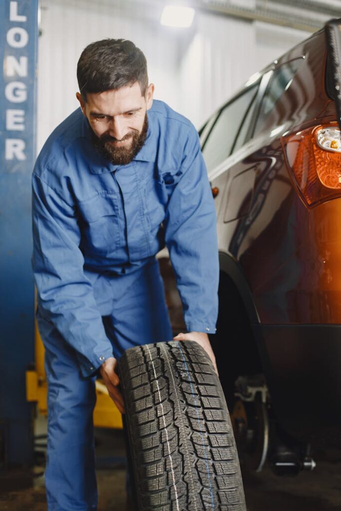 A mechanic in blue overalls adjusts a tire in a car service garage.