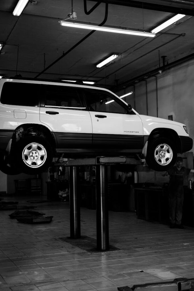 Black and white photo of a Subaru SUV lifted in an auto repair shop.